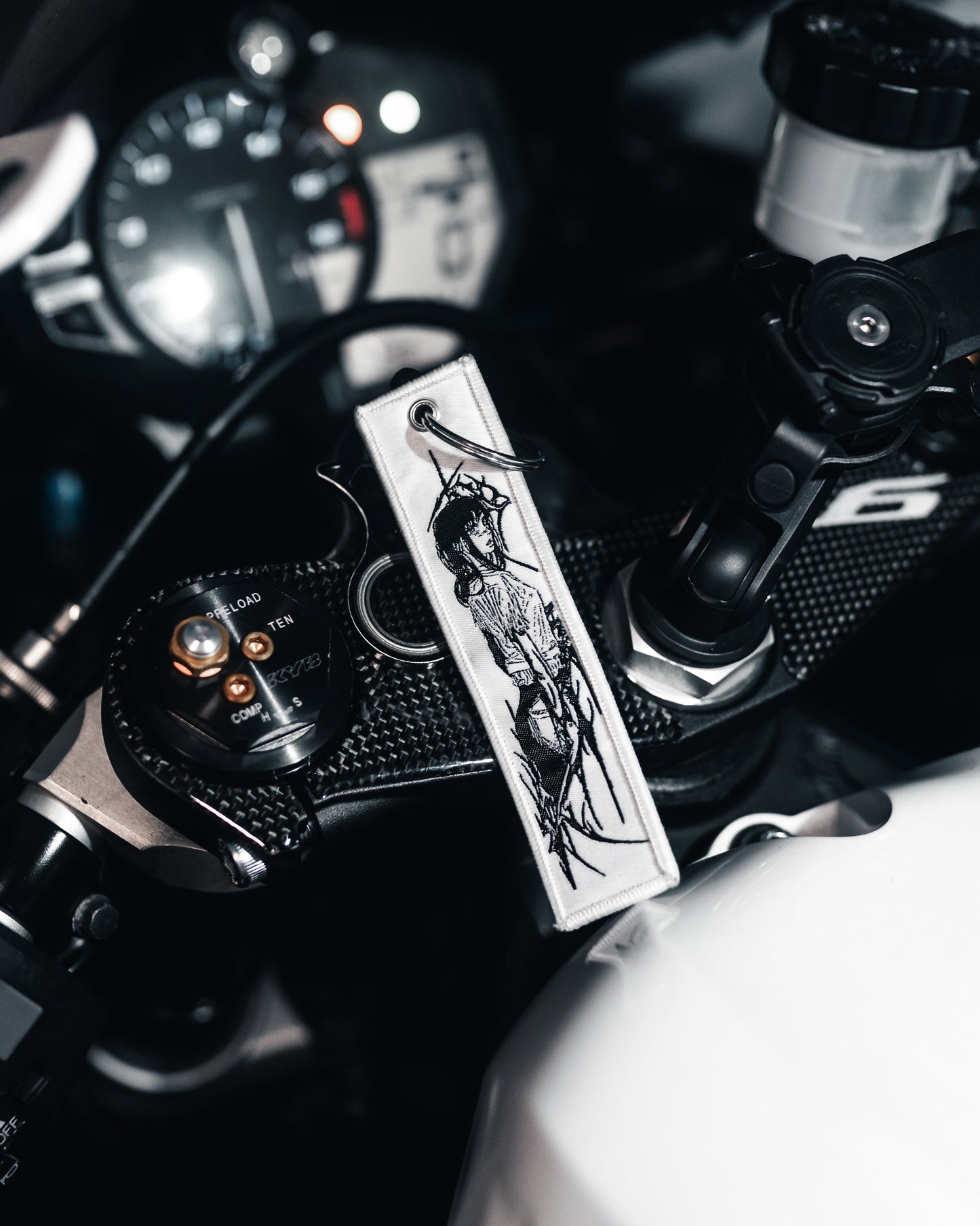 Close-up of a motorcycle handlebar with a decorative keychain and brand logo.